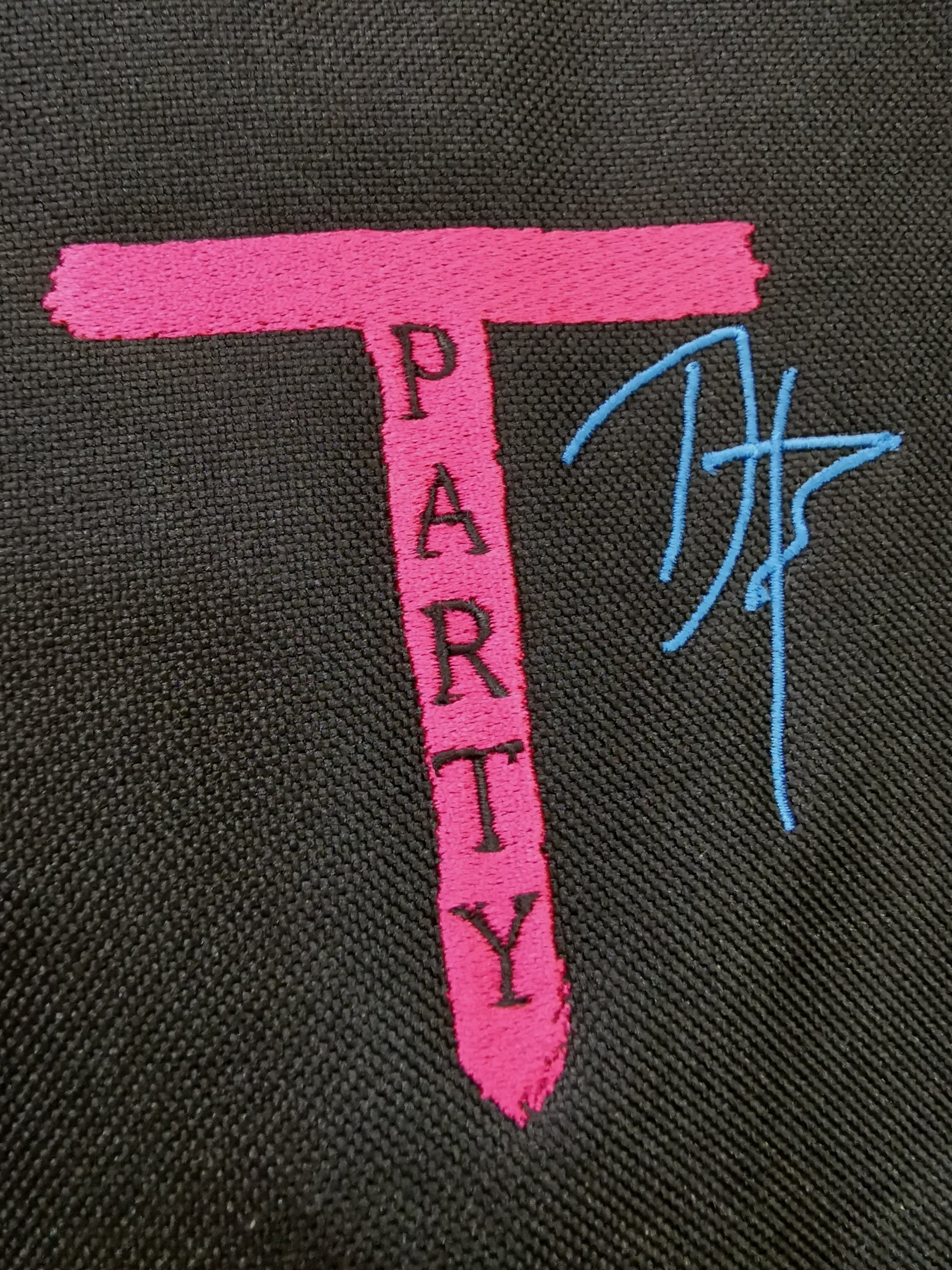 Pink embroidered text spelling ’PARTY’ with a blue signature or initials next to it.